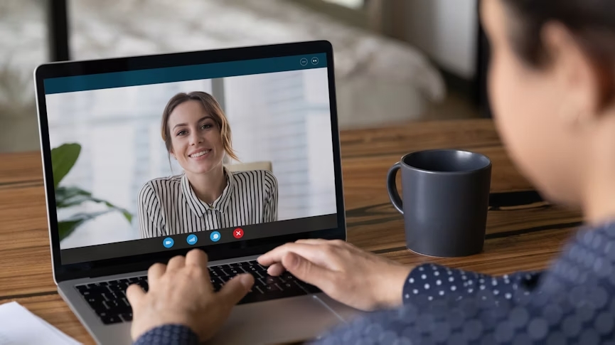 Eine lächelnde Frau blickt jemandem beim Videochat vom Bildschirm des Laptops entgegen.
