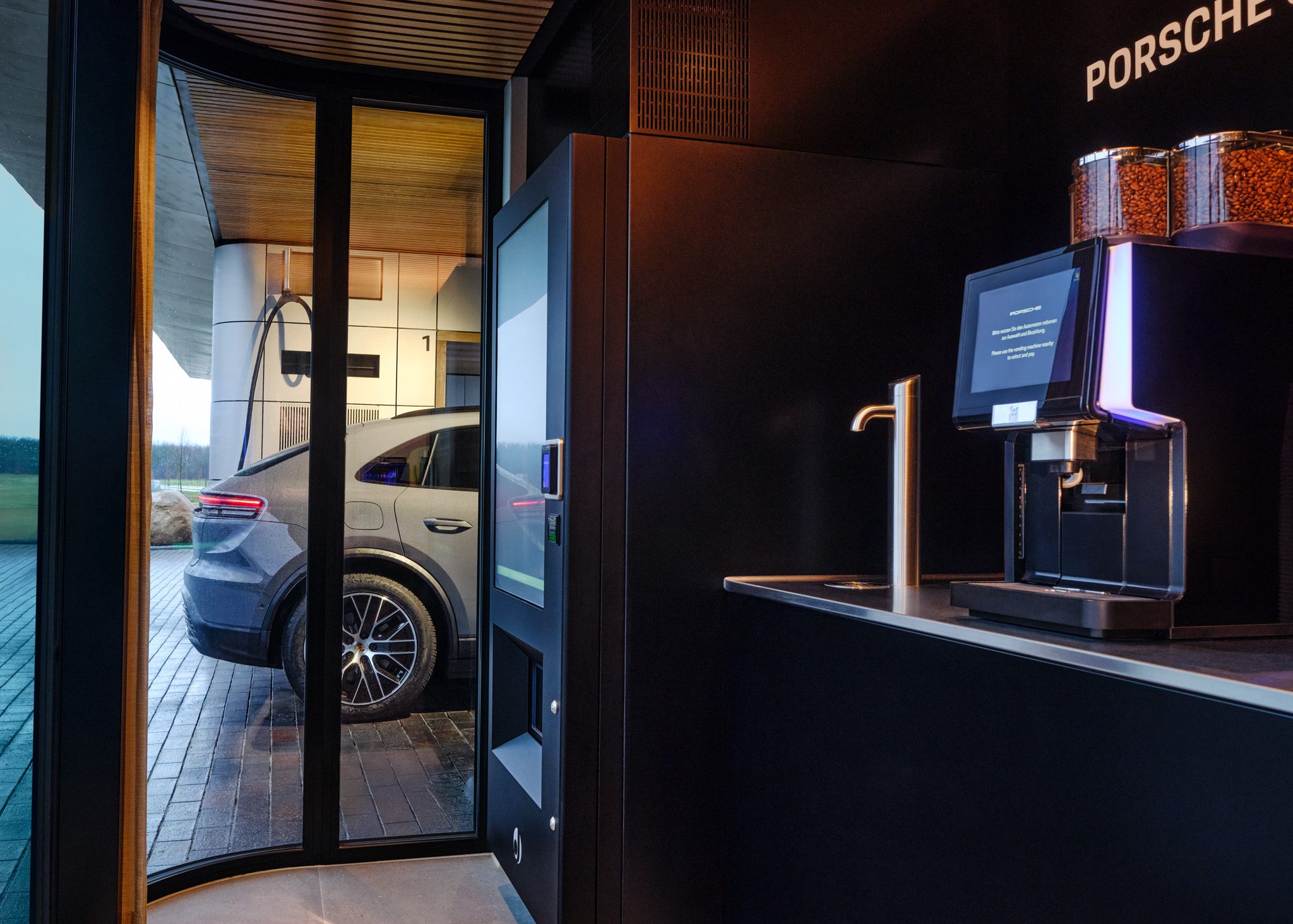 Porsche electric SUV charging at premium EV station, viewed from lounge with coffee machine. Luxury charging hub combining fast charging, comfort, and sustainable mobility for modern electric vehicle drivers.