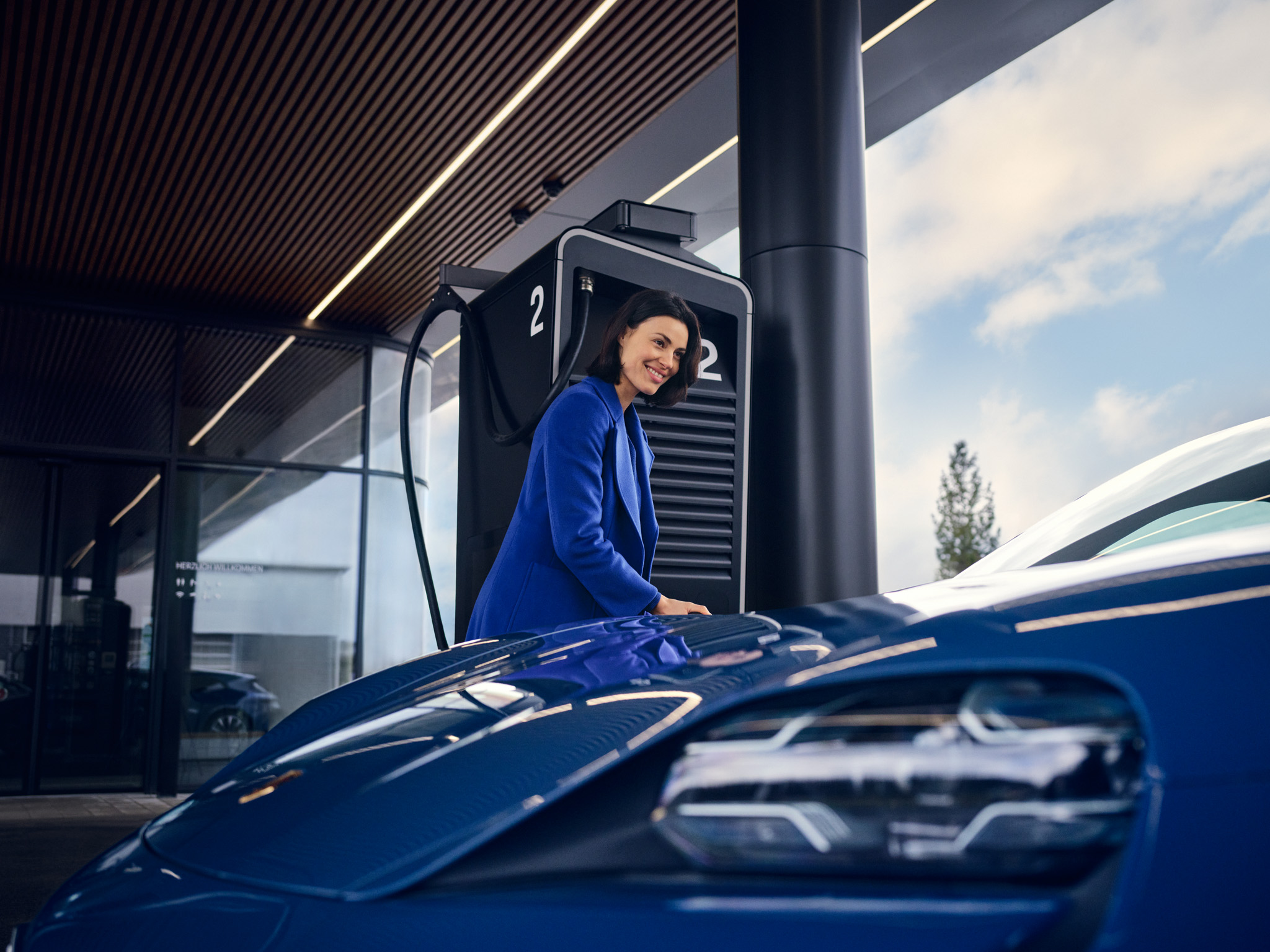 A woman charges her blue Porsche Taycan at an HPC Charging Lounge.
