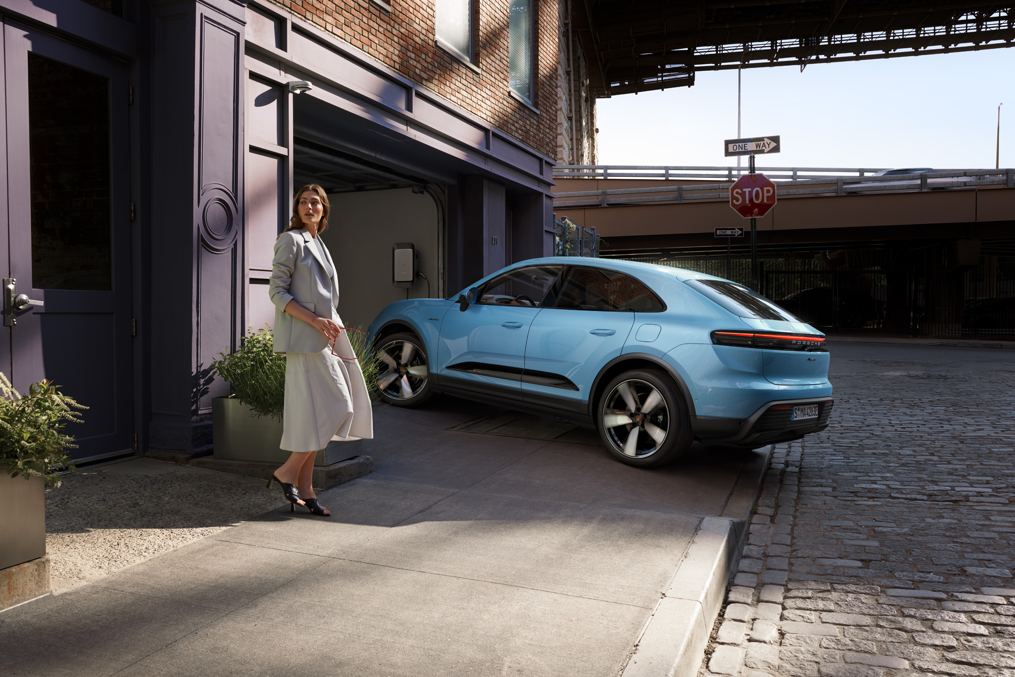 Stylish woman with Porsche electric SUV in blue, parked at modern urban garage with EV charger. Premium electric mobility, sustainable lifestyle, and luxury car design for city driving and home charging convenience.