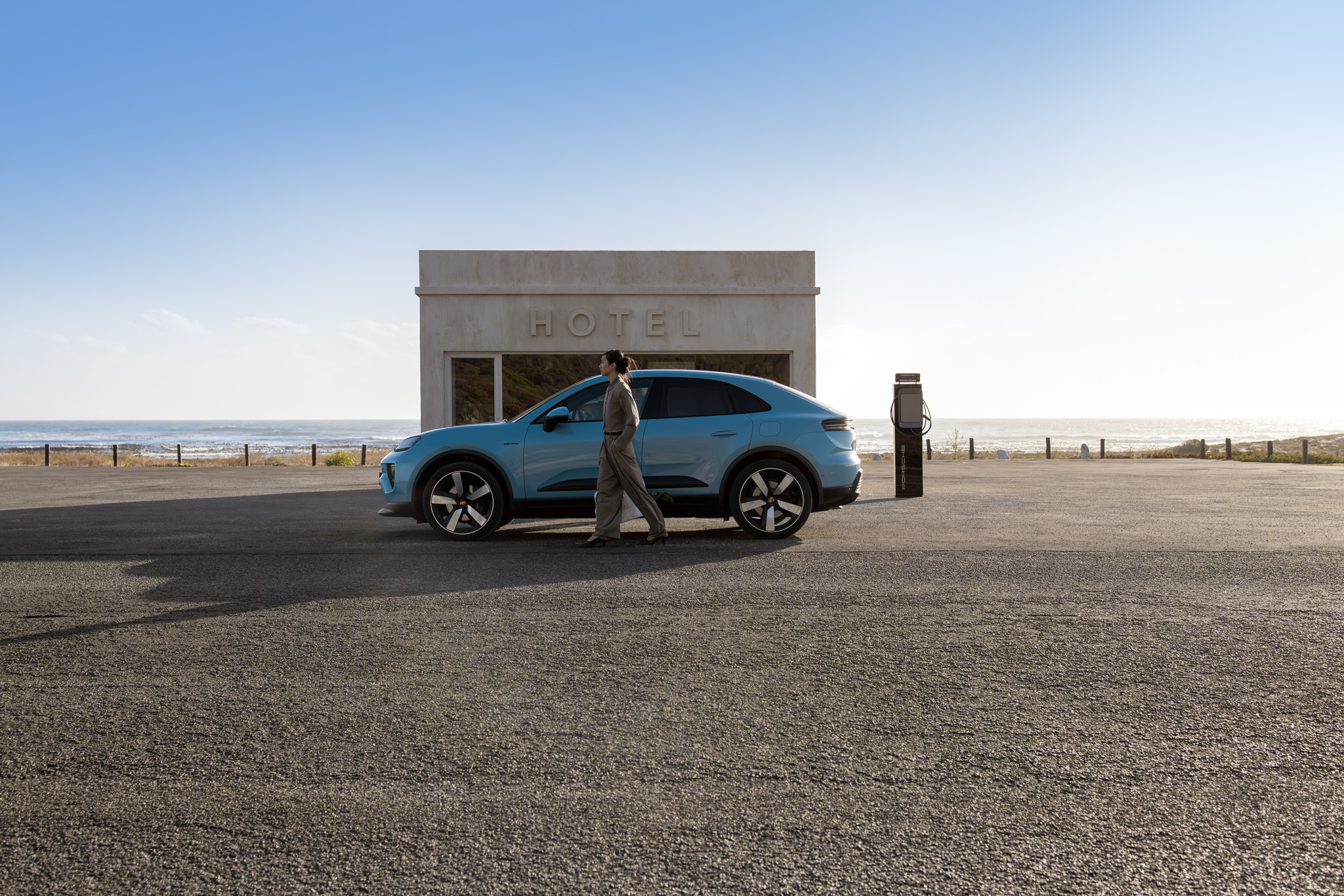 Blue Porsche electric SUV charging at hotel EV station by the seaside. Luxury electric mobility meets sustainable travel with convenient destination charging for premium electric cars on road trips and coastal getaways.