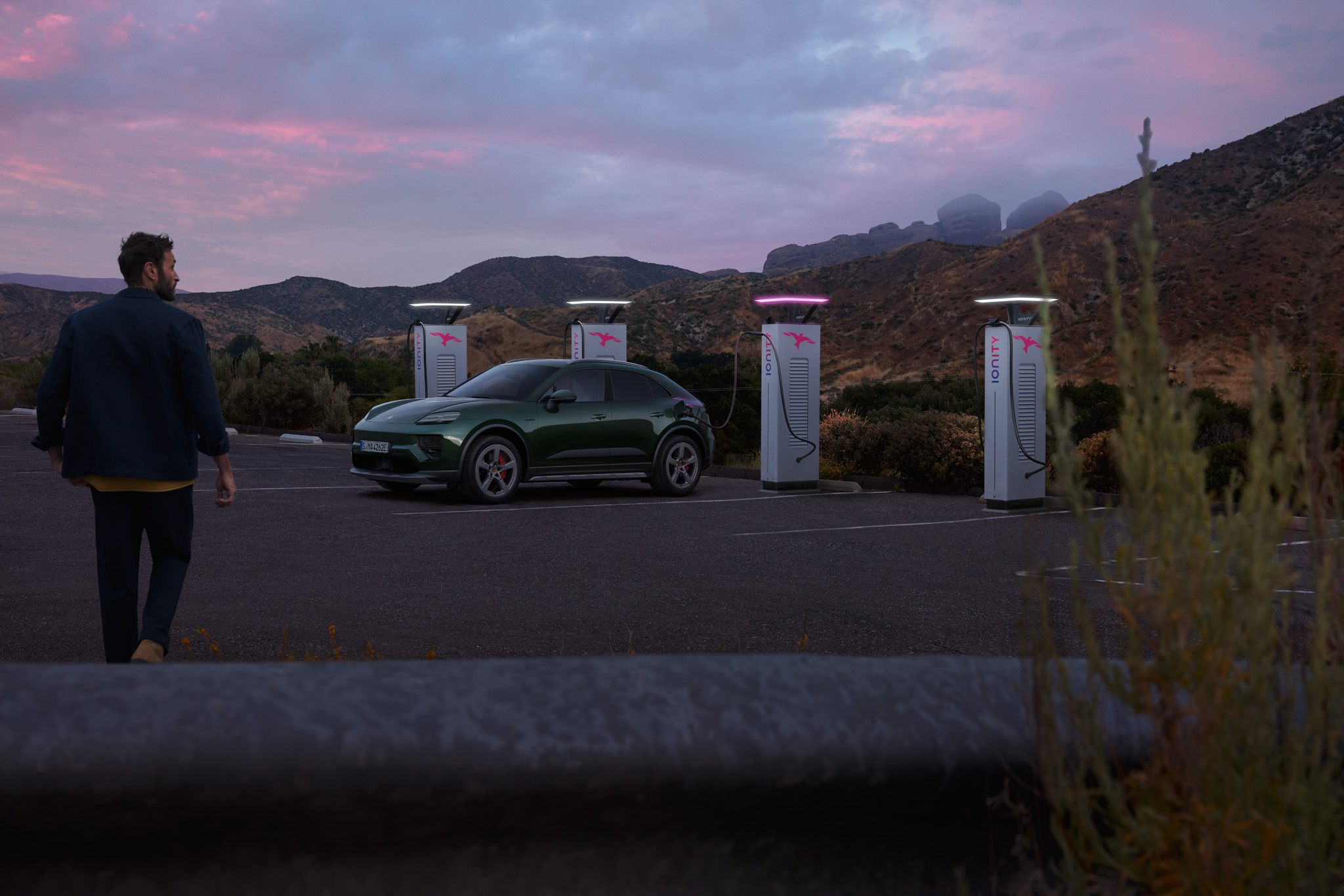Green Porsche electric SUV charging at ultra-fast EV charging station in scenic mountain landscape at sunset. Luxury electric car, sustainable travel, and fast-charging technology for long-distance journeys.