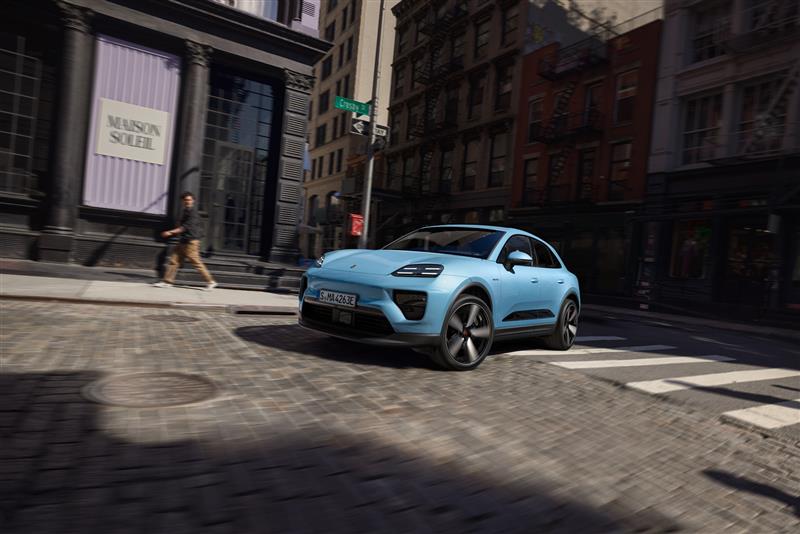 A blue Macan Electric drives over a zebra crossing in a bend and a person turns to look at the vehicle.