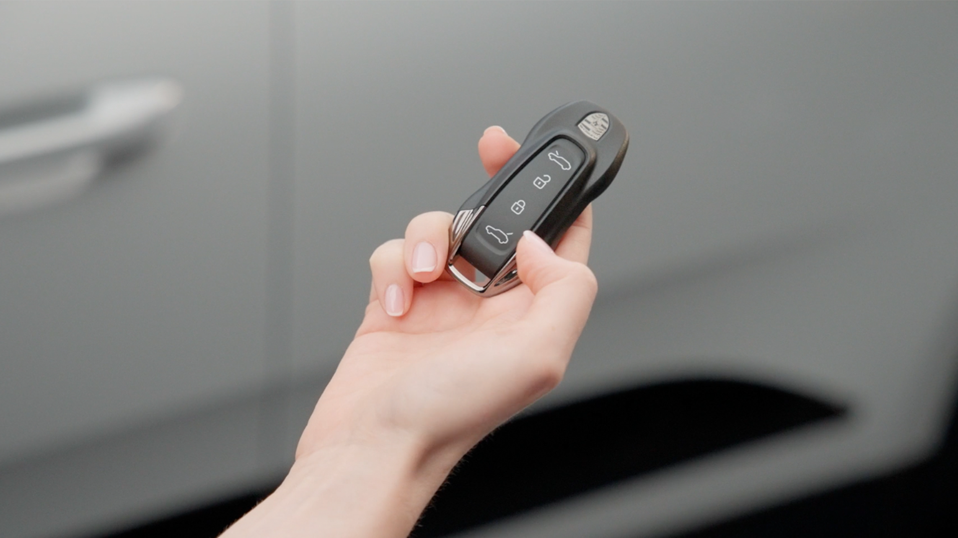 A Porsche vehicle key in the hand of its owner in front of the corresponding vehicle.